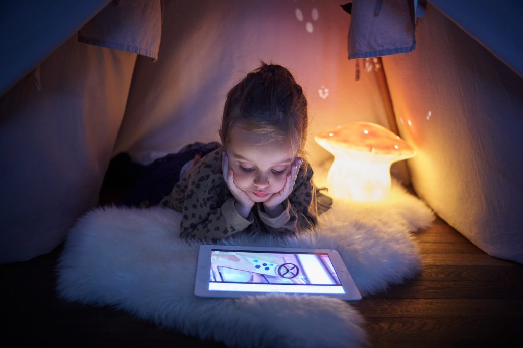 Petite fille allongée dans un tipi et qui regarde sa tablette de façon intéressante