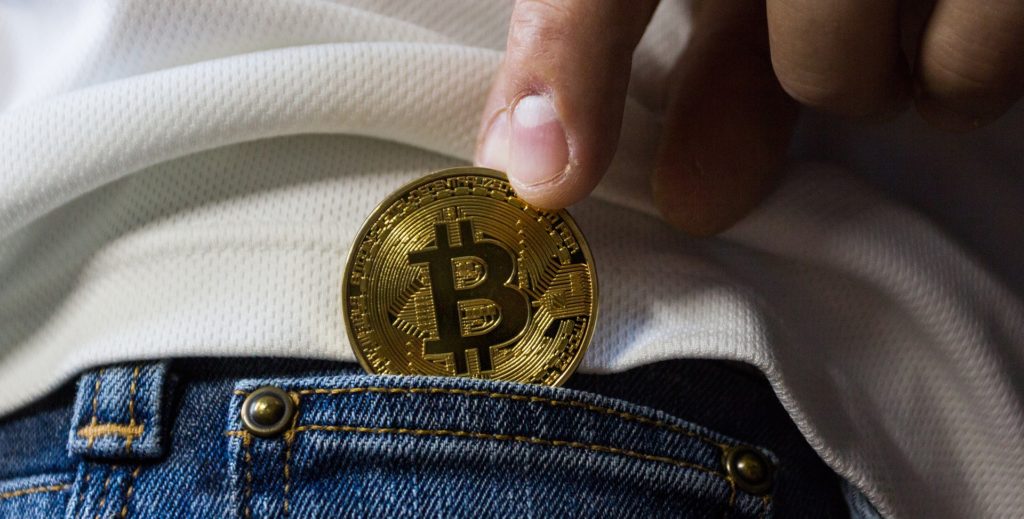 Vu d'une poche de jeans dans laquelle la personne insère un bitcoin sous forme de pièce de monnaie