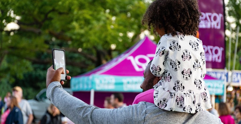 Un papa avec sa fille sur les épaules qui se prennent en selfie avec le smartphone