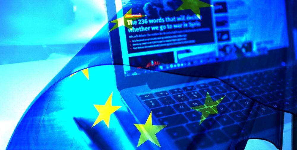 fake-news-europe Un ordinateur ouvert avec un site d'informations à l'écran et un drapeau de l'Europe en filigrane sur toute l'image