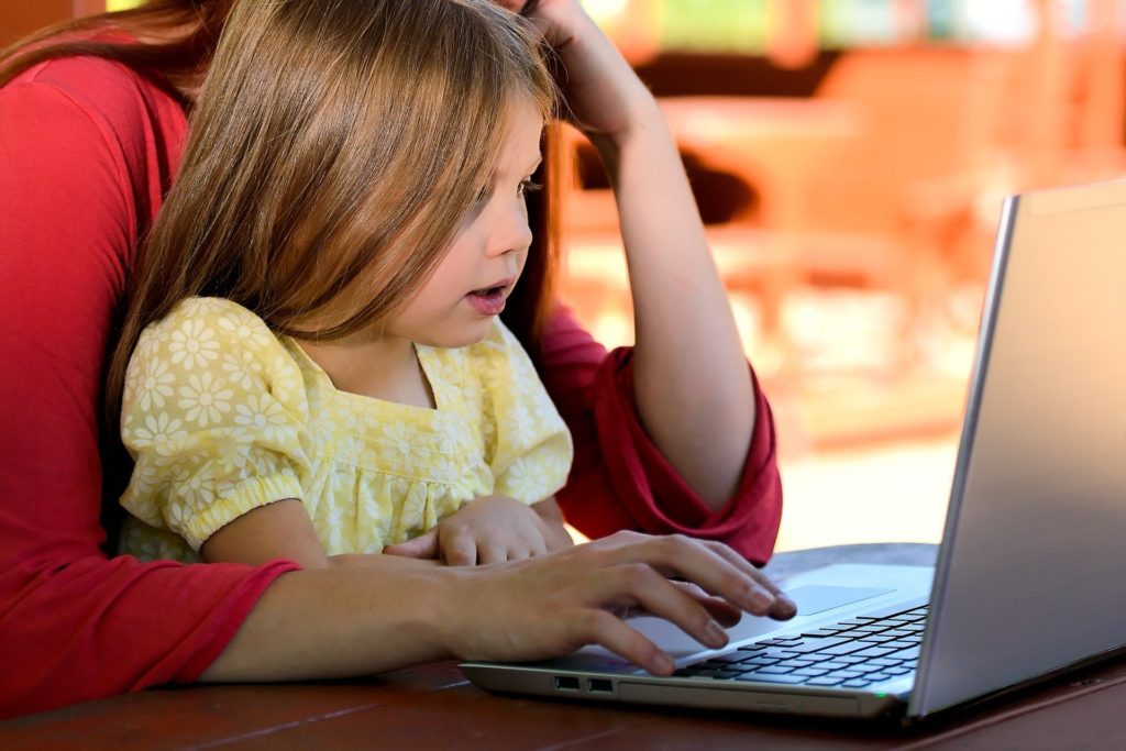 Foto eines Kindes auf dem Schoß eines Erwachsenen, die zusammen einen Computerbildschirm betrachten