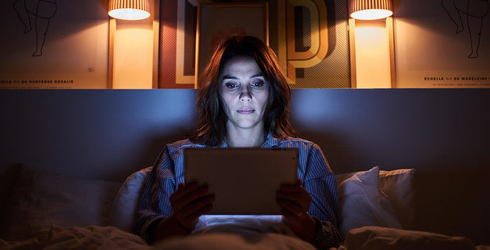 Une femme dans son lit la nuit avec une tablette dans les mains et regardant l'écran