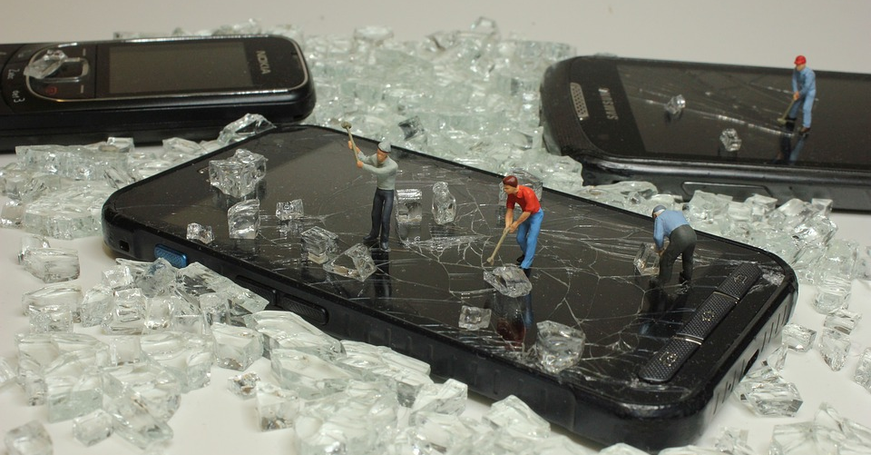 Des smartphones au milieu de verre cassé avec des mini figurines dessus