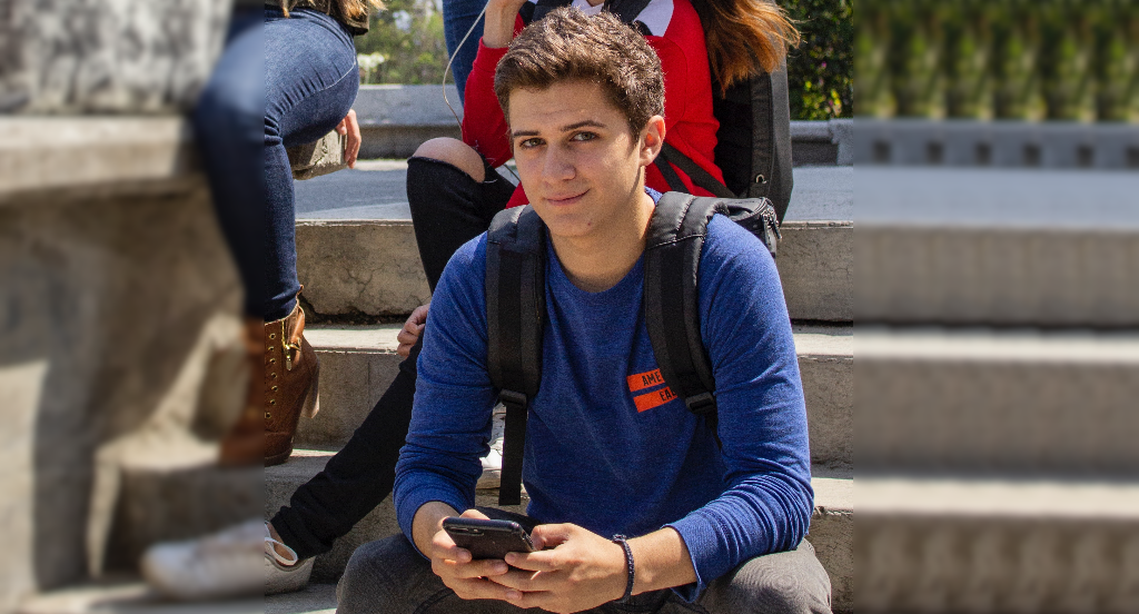 Jeunes assis sur des escaliers avec au centre un garçon qui regarde en face de lui et tiens un smartphone dans ses mains