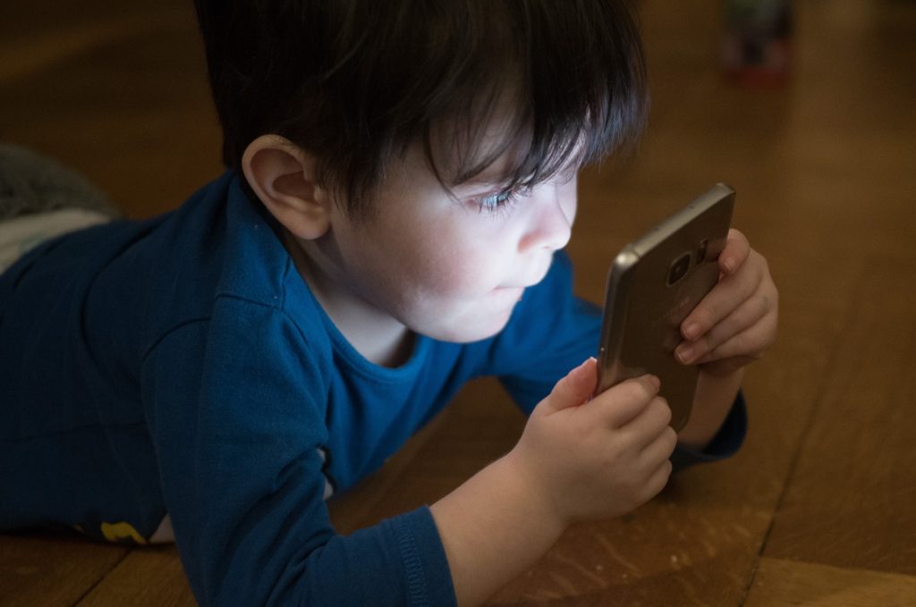 Kleiner Junge der sein Handy sehr nah ans Gesicht hällt und konzentriert darauf schaut