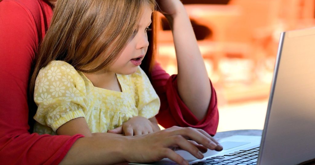 Photo d'un enfant sur les genoux d'un adulte en train de regarder un écran d'ordinateur