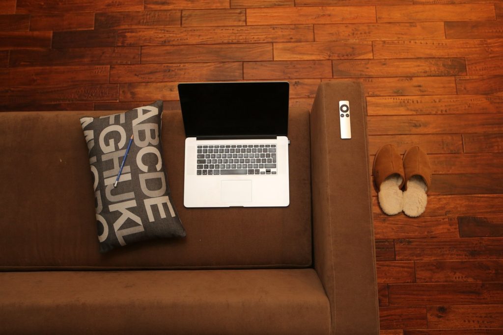 home-office Vogelperpektive auf ein Laptop was auf dem Sofa ist mit Hausschuhen daneben