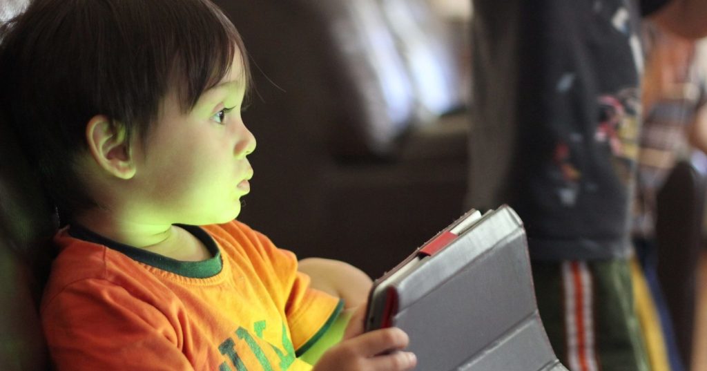 Photo d'un jeune enfant avec le regard vide tenant une tablette dans ses mains