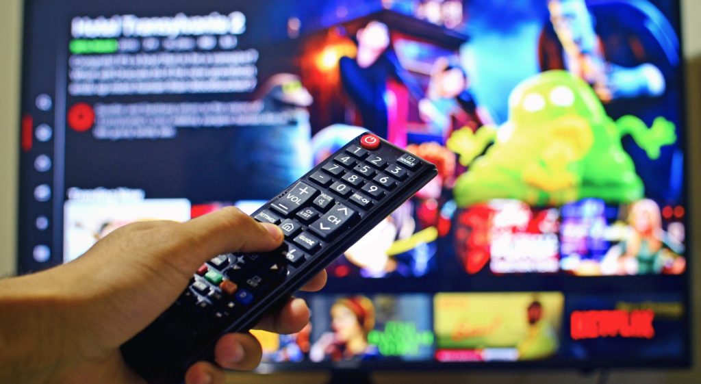 Fernbedienung die auf einen Fernsehbildschirm zeigt wo Netflix läuft