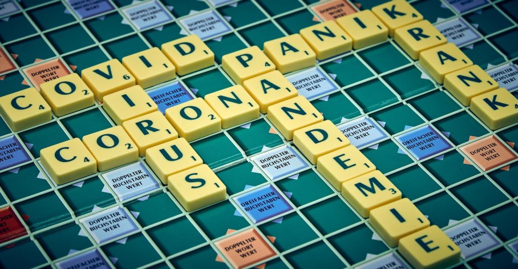 Ein Scrabblebrett auf dem Folgende Wörter gelegt sind: COVID; VIRUS; CORONA; PANDEMIE; PANIK; KRANKHEIT