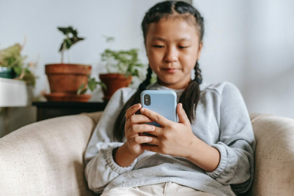 Une enfant est assie sur un fauteuil en regardant son smartphone.