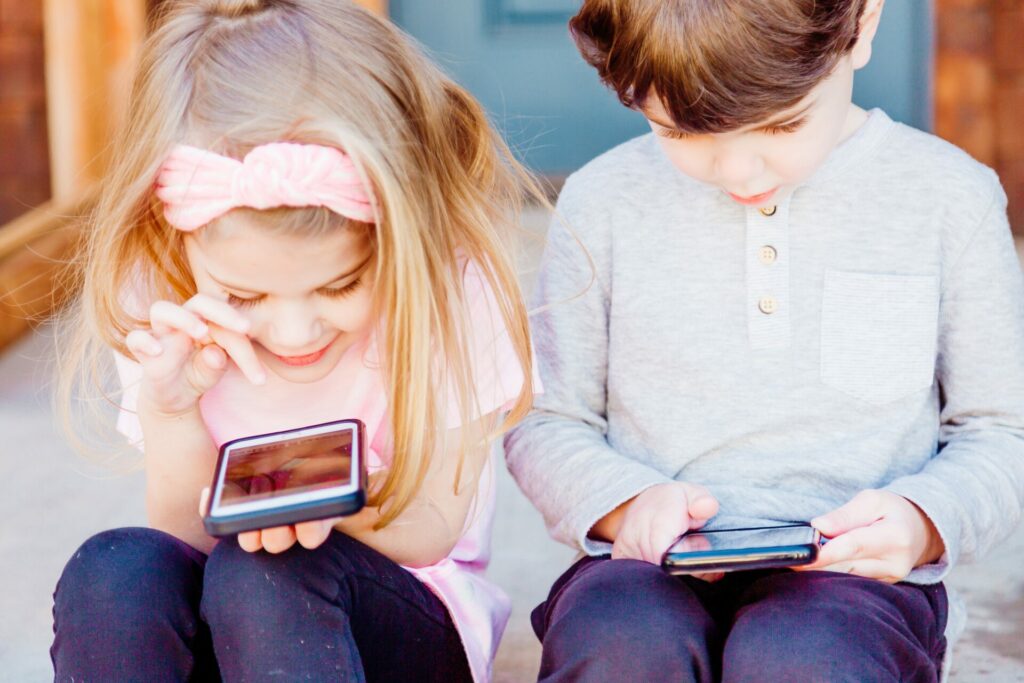 Ein kleines Mädchen und ein kleiner Junge die sitzend auf einer Treppe sind, spielen mit ihren Smartphones.